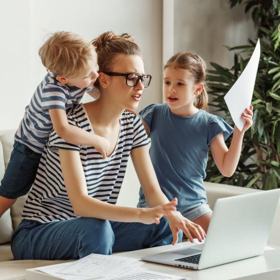 Stressad mamma med två barn jobbar hemma framför skärm