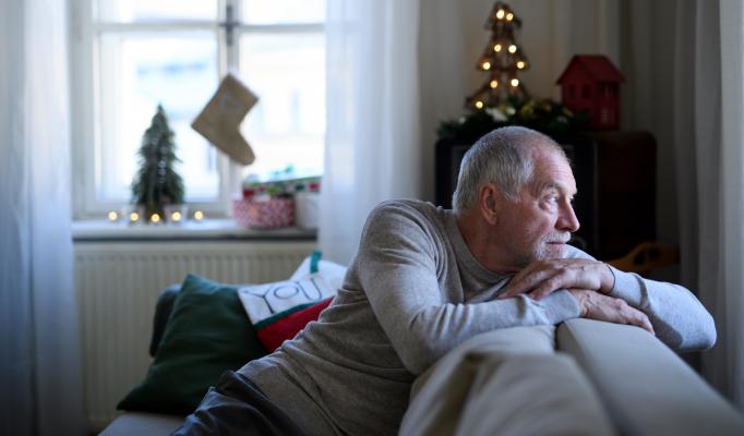 En man sitter ensam i soffan och tittar ut genom fönstret