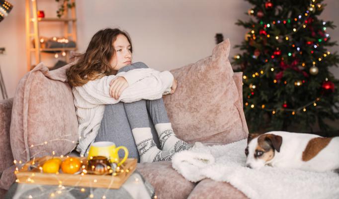 Flicka sitter ensam i soffan med en hund bredvid