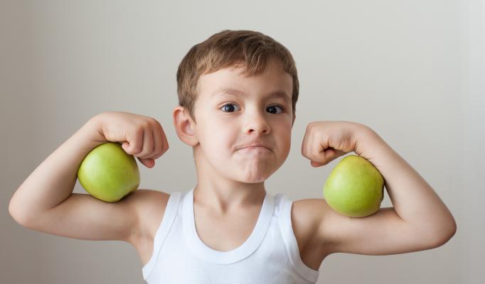 Liten pojke har två gröna äpplen som biceps på sina armar