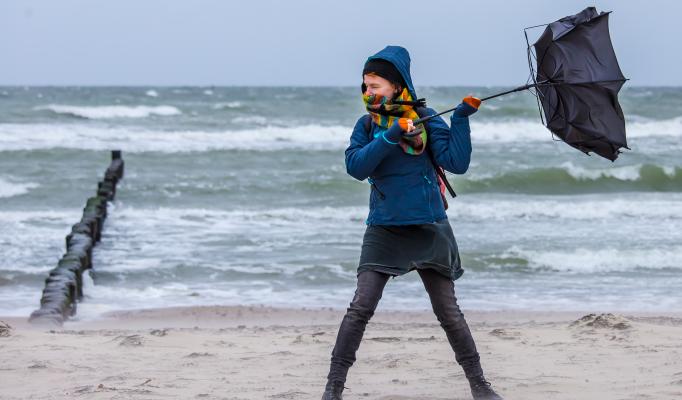 Kvinna står och håller i ett paraply på en strand i stormigt väder Kvinna står och håller i ett paraply på en strand i stormigt väder