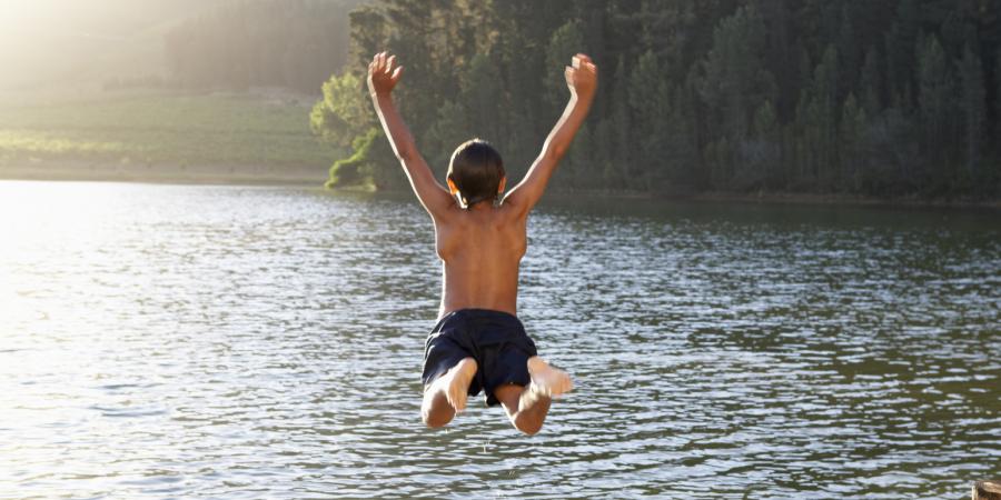 Barn hoppar från brygga ner i vattnet